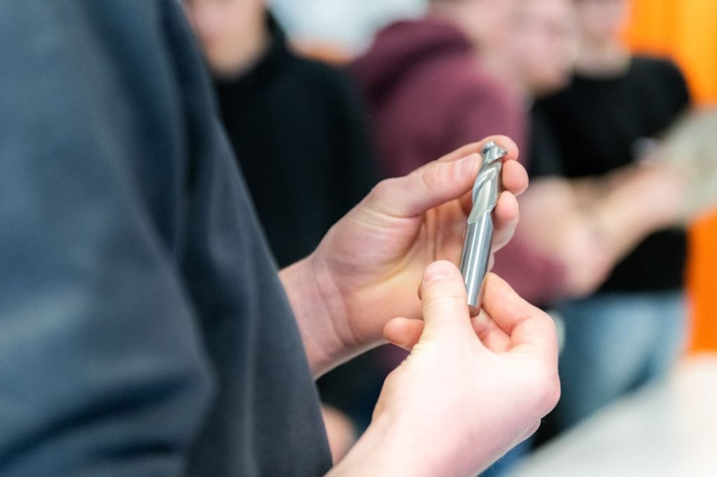 our-story Hands carefully examining a metal drill bit during a workshop session.